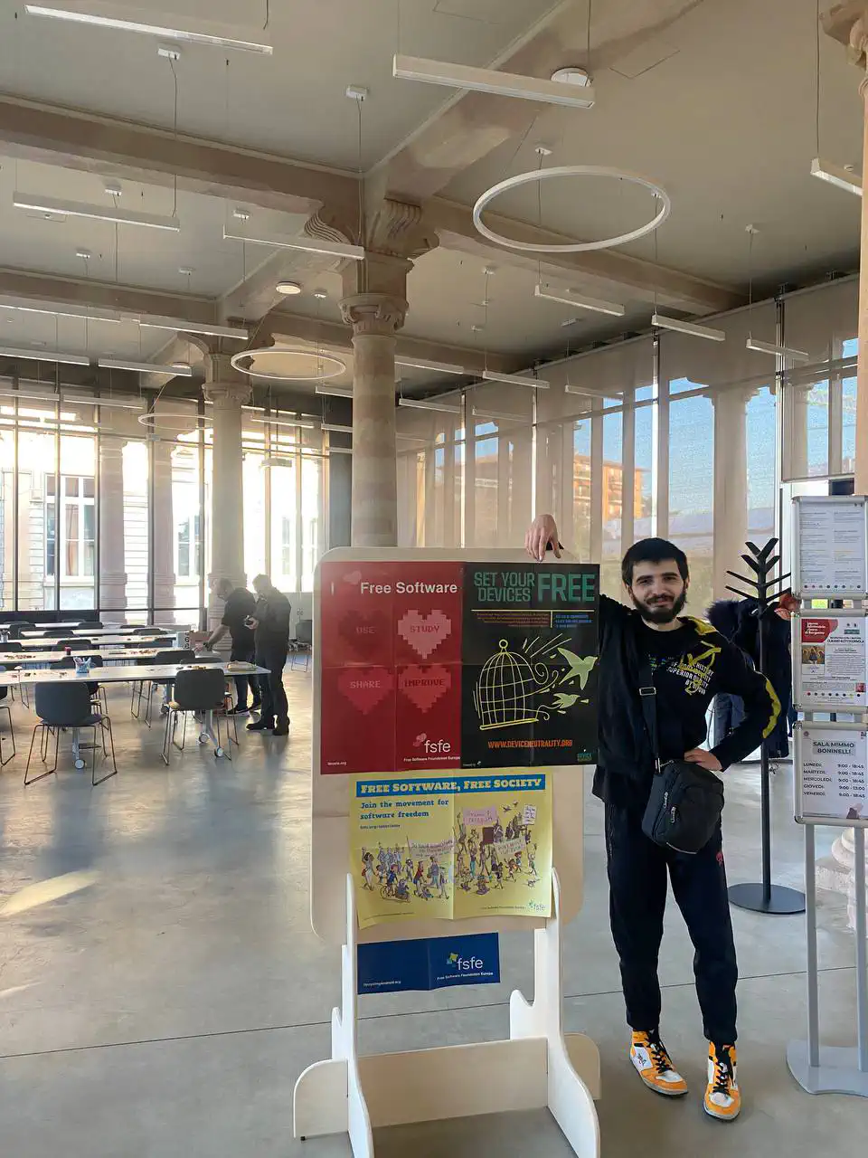 Un Andrea Laisa selvatico in posa prima dell’evento e a fianco di una bacheca con i poster della FSFE